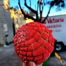 Una concha roja sostenida frente a la panadería.