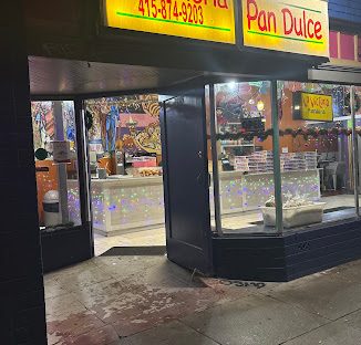 La Victoria storefront glowing at night, with the open entrance and pastry cases visible.