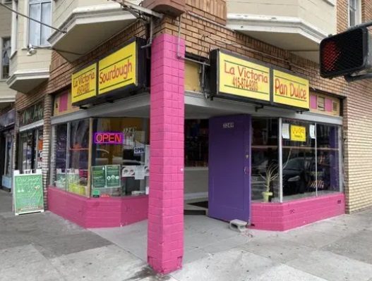 La Victoria street-corner storefront with a bright pink facade and La Victoria, Sourdough, and Pan Dulce signs.